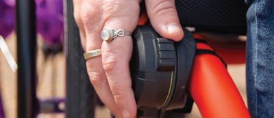 Hand with a ring holding onto a black handlebar with red accents, blurred background